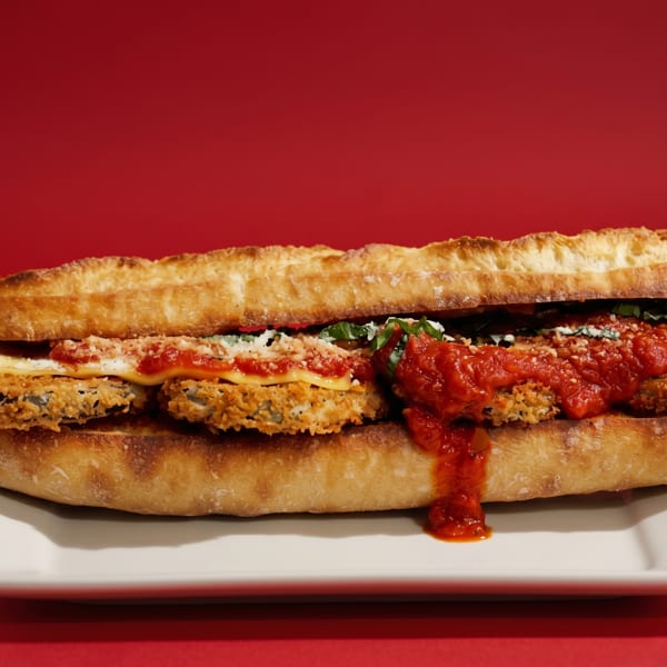 A large fried eggplant parmesan sandwich with marinara sauce and cheese on a white plate.