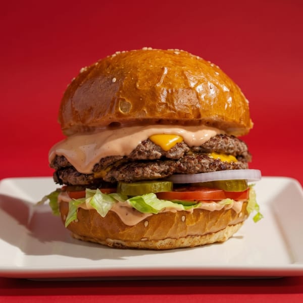 A double cheeseburger with special sauce, lettuce, tomato, pickles, and onions on a white plate.